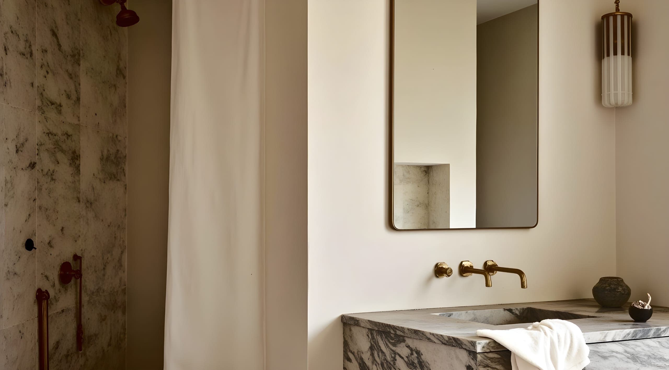 A marble basin with an unlacquered brass tap under a bronze-framed mirror