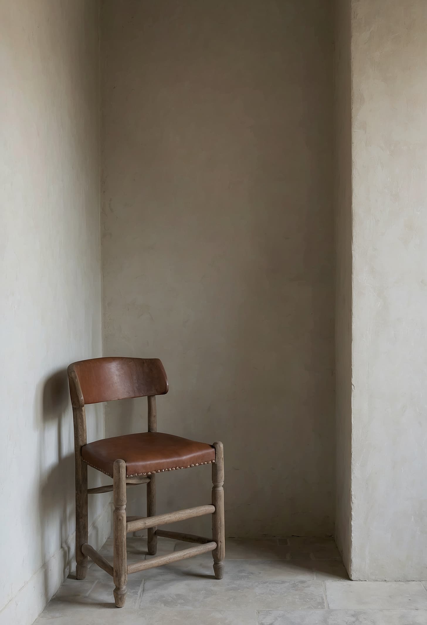 A linen armchair beside a deep stone window, afternoon sun on rough plaster walls